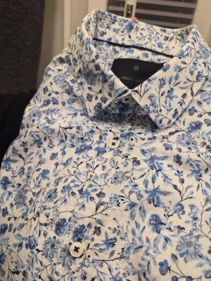 Blommig skjorta från Jack & Jones Premium Xl 44 - Snygg skjorta från Jack & Jones med blått blommönster på vit botten. Skjortan har klassisk krage, knäppning framtill och långa ärmar. Perfekt för dig som vill sticka ut med en fräsch och trendig look.