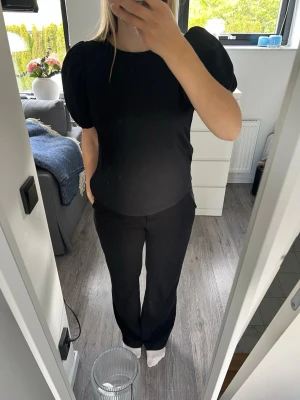 Svart topp med puffärmar - Säljer en svart topp med puffiga kortärmar och rund hals. Toppen har en enkel, stilren design och är gjord i ett mjukt material som känns skönt mot huden. Från Vero Moda i storlek S. Använd men i bra skick!