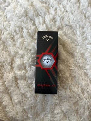 Callaway Diablo golfboll i ask - Säljer en Callaway Diablo golfboll i originalförpackning. Asken är svart med röda detaljer och har Callaway-loggan tydligt synlig. Perfekt för golfentusiasten som vill ha en kvalitetsboll från ett känt märke.