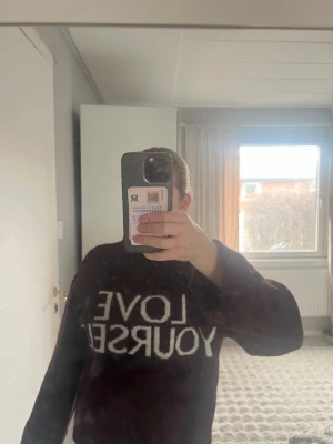 Vinröd stickad tröja med text - Mysig vinröd stickad tröja med polokrage och vit text 'LOVE YOURSELF' framtill. Tröjan har en avslappnad passform och ribbade muddar vid ärmslut och nederkant. 
