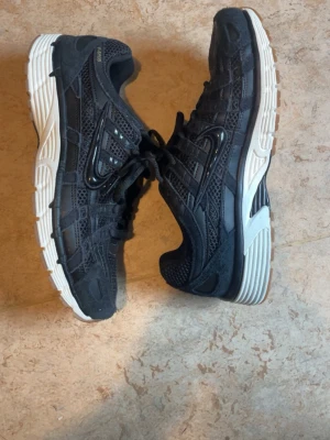 Nike svart p6000 - Svarta sneakers från Nike med mesh- och syntetpaneler, vita och bruna sulor samt klassisk Swoosh-logga på sidan. Skorna har snörning och sportig design som passar till streetwear och avslappnade outfits.