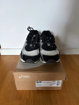 ASICS GEL-NYC svart/vit sneakers - Snygga ASICS GEL-NYC sneakers i svart och vitt med silvriga detaljer. Skorna har en chunky sula och ovandel i mesh och syntetmaterial. Perfekta för dig som gillar sportig och trendig stil. Klassisk snörning och bekväm passform.