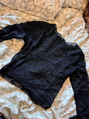 Svart spetsblus med lång ärm - Säljer en svart blus i genombruten spets med lång ärm. Toppen är transparent och har ett romantiskt uttryck med fina spetsdetaljer över hela plagget. Perfekt att styla lager på lager för en trendig look. Oanvänd men köpt för något år sedan💕