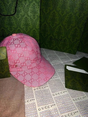 Rosa keps från Gucci med GG-mönster - Säljer en rosa keps från Gucci med ikoniskt GG-monogram i hela tyget. Kepsen har böjd skärm och klassisk sexpanelsdesign. Tillverkad i ett tygmaterial med tydlig struktur och exklusiv känsla. Perfekt för dig som vill sticka ut med en lyxig accessoar. Splitterny för mer info pm
