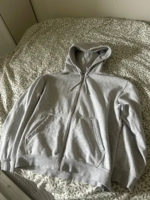 Grå zip-hoodie från Weekday - Snygg gråmelerad hoodie från Weekday med dragkedja framtill, huva med dragsko och två stora fickor. Perfekt för en chill och avslappnad stil. Tillverkad i mjukt material som känns skönt mot huden.