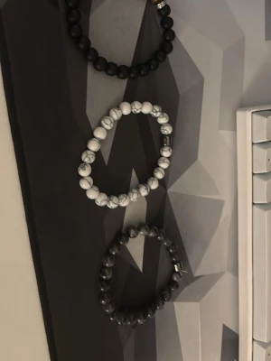 Set med tre pärlarmband i olika färger - Säljer ett set med tre elastiska armband med runda pärlor. Ett armband är svart, ett är vitt med grå marmorering och ett är mörkgrått med marmorerad effekt. Perfekta att mixa och matcha för en cool och stilren look.