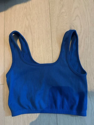 Ribbad blå bodytop - Snygg ribbad bodytop i djupblå färg med breda axelband och rundad halsringning. Perfekt att styla under skjortor eller som den är. Mjuk och stretchig känsla för extra komfort.