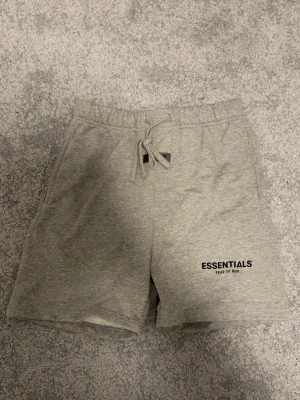 Grå shorts från Essentials Fear of God - Snygga grå shorts från Essentials Fear of God med snörning i midjan och logga tryckt på vänster ben. Mjukt material och avslappnad passform.