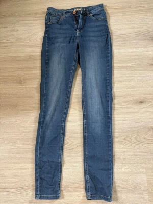 Mörkblå skinny jeans från Denim - Snygga mörkblå skinny jeans från Denim med klassisk femficksdesign och lätt slitna detaljer på låren. Jeansen har normal midja och smal passform hela vägen ner. Perfekta för en avslappnad och trendig look.