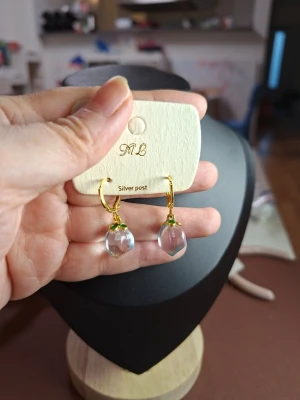 Guldiga örhängen med klara droppar - Snygga örhängen från ML med guldfärgade ringar och klara, droppformade hängen i glasliknande material. Perfekta för att ge en elegant touch till din stil. Silver post för bekväm användning.