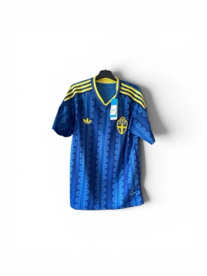 Sverige VM tröja-2026 - Säljer en riktigt snygg Adidas Sverige-tröja. Blå med gula detaljer och unikt mönster över hela tröjan. Perfekt för samlare, fotbollsfans eller dig som vill ha en clean streetwear-look.  * Märke: Adidas Originals * Landslag: Sverige * Skick: Helt ny med tags kvar * Färg: Blå/Gul * Passform: Regular fit * Väldigt fin kvalitet och detaljer  Perfekt till matcher, sommaren eller som en snygg vardagströja.  📩 Skriv vid intresse eller frågor!