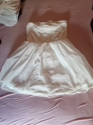 Vit axelbandslös kort klänning - Söt vit axelbandslös klänning med voluminös kjol och lätt rynkad överdel. Klänningen är kort och har ett tunt, skirt tyg som ger en luftig känsla. Perfekt för sommarens alla tillfällen. Pris kan diskuteras🫶🏼