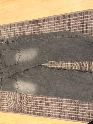 Flared jeans  - Säljer ett par grå jeans med raka ben och slitna detaljer vid knän och benslut. Jeansen har klassiska fem fickor och en snygg tvättad look med ljusare partier framtill och baktill. Perfekta för en avslappnad och trendig stil.
