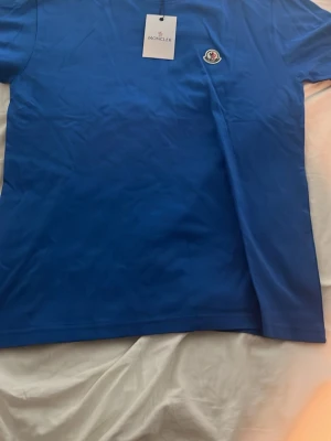 Blå Moncler t-shirt i bomull - Snygg blå t-shirt från Moncler med klassisk rund hals och Moncler-logga på bröstet. Tillverkad i mjuk bomull och har en enkel, stilren design som passar perfekt till jeans eller shorts. Passar perfekt på någon som använder storlek M