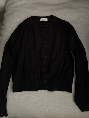 Svart basic kofta med knappar från hm - En enkel svart kofta med rund hals och knäppning framtill. Långärmad modell i mjukt, tunt material som passar perfekt till lager på lager. Stilren och lättmatchad till alla outfits.