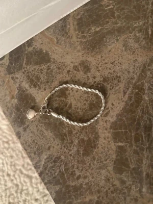 Flätat silverfärgat armband från Snö of Sweden - Snyggt armband i silverfärg med flätad kedja. Armbandet har ett klassiskt karbinlås och passar perfekt för dig som gillar stilrena accessoarer. Materialet ser ut att vara metall och designen är enkel men trendig.
