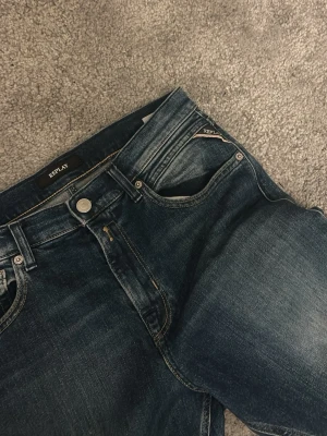 Mörkblå Replay jeans med tvättade detaljer - Säljer ett par mörkblå jeans från Replay med snygga tvättade detaljer och klassisk femficksmodell. Jeansen har raka ben och är tillverkade i ett slitstarkt denimtyg. Perfekta för dig som gillar en avslappnad men ändå stilren look.
