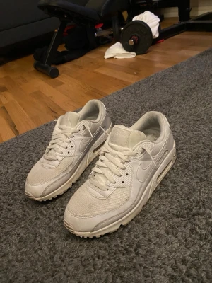 Nike Air Max 90 vita sneakers - Fräscha Nike Air Max 90 sneakers i helvitt med klassisk siluett. Ovandelen är i en mix av mesh och läder med tydliga Air Max-detaljer på sulan. Perfekta för dig som gillar stilrena och sportiga skor med retrovibbar.