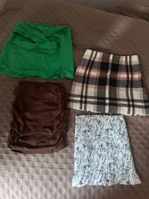 Fyra trendiga kjolar i olika stilar - Säljer fyra kjolar: en grön omlottkjol, en brun kjol med rynkade sidor, en kort rutig kjol i beige, svart och rött samt en vit blommig kjol med volangkant. Perfekt för dig som vill variera din stil med färg, mönster och olika material. Storlekarna XS, S och M men alla har passat mig som normaltsätt är S🌸