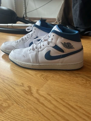 Nike Air Jordan 1 Mid vit/blå - Säljer ett par Nike Air Jordan 1 Mid sneakers. Andvända typ 5 gånger, bara lite creasade men annars väldigt fräscha. Köpte dom för 1800. Möta upp i Stockholm.( har kvar låda om man vill ha med)