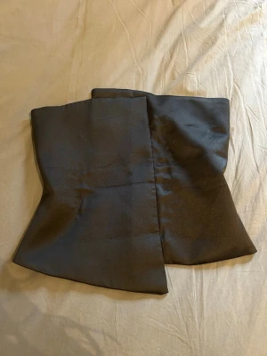 Svart satinliknande korsett - Stilren svart korsett i satinliknande material med dragkedja bak. Modellen har en lätt utsvängd form och är utan synliga detaljer eller mönster. Perfekt för att skapa en snygg siluett och passar till många olika looks.