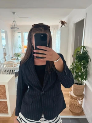 Svart kavaj med vita ränder Brandtex - Snygg svart kavaj från brandtex med tunna vita kritstrecksränder. Klassisk modell med slag, en knapp framtill och två fickor med lock. Perfekt för en stilren look. Materialet är mjukt och har en lätt struktur. Uppskattar storleken till M/L
