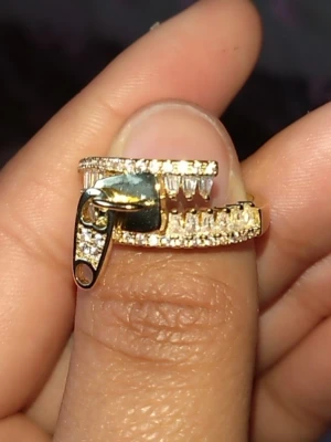 Guldfärgad ring med dragkedjedesign - Säljer för att jag har en till. Använd en gång. Unik guldfärgad ring med glittrande diamanter och en cool dragkedjedetalj framtill. Ringen har två rader av små gnistrande stenar och en rörlig dragkedja i metall som ger en edgy och trendig look. Perfekt för dig som gillar statement-smycken och vill sticka ut. 7cm runt om📏 