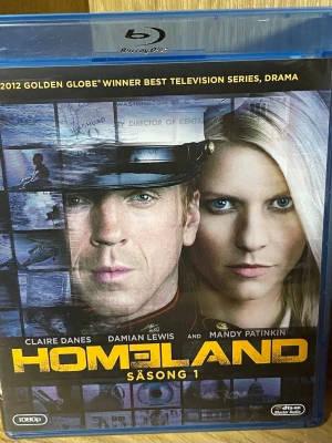 Homeland Säsong 1 Blu-ray Box - Homeland Säsong 1 på Blu-ray med 3 skivor och totalt 12 avsnitt. Serien är en spännande action/drama med Claire Danes, Damian Lewis och Mandy Patinkin i huvudrollerna. Omslaget är blått med gul text och bilder från serien. Extramaterial ingår.