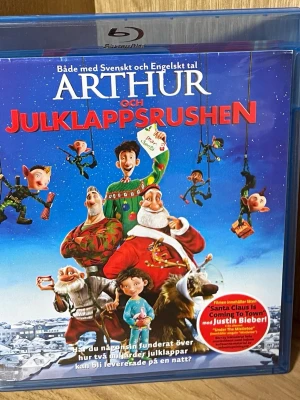 Blu-ray: Arthur och Julklappsrushen - Blu-ray-film 'Arthur och Julklappsrushen' med både svenskt och engelskt tal. Omslaget är färgglatt med julmotiv och karaktärer från filmen. Innehåller bonusmaterial som bakom kulisserna, musikvideor och animeringsinslag. Perfekt för julmys och familjekvällar.