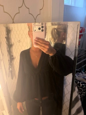 Svart v-ringad blus med volymärmar - Snygg svart blus med djup v-ringning och voluminösa långa ärmar. Blusen har en lös passform och faller fint över kroppen. Perfekt att styla med jeans eller kjol för en trendig look.