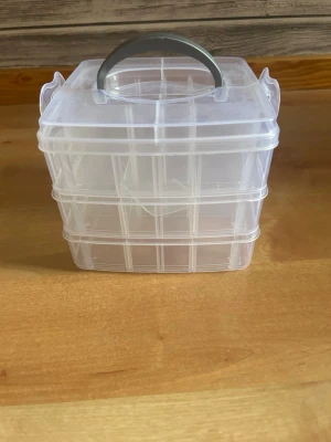 Transparent förvaringslåda med handtag - Praktisk transparent förvaringslåda i plast med tre stapelbara fack och ett smidigt handtag upptill. Perfekt för att organisera småprylar, smycken eller pysselgrejer. Lådan har smarta lås på sidorna som håller facken på plats.