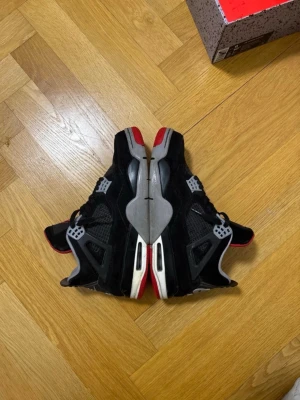 Air Jordan 4 bred - Säljer ett par Air Jordan 4 sneakers i svart mocka med röda och grå detaljer. Klassisk siluett med meshpaneler, plastdetaljer och synlig Air-sula. Ikonisk Jumpman-logga på plösen och bekväm vadderad insida. Perfekta för dig som gillar streetwear och sneakerskultur.