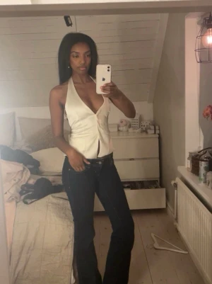 Vit omlott halterneck topp - Snygg vit omlott topp med djup v-ringning och halterneck. Toppen är ärmlös och har öppen rygg med knytband i ryggen. Perfekt för dig som vill ha en trendig och stilren look.