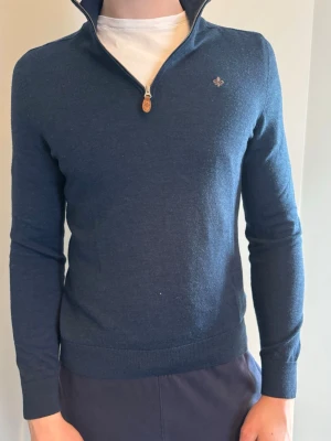 Mörkblå stickad tröja från Morris - Snygg mörkblå stickad tröja från Morris med halv dragkedja och liten broderad logga på bröstet. Tröjan har ribbade muddar och hög krage. Perfekt för dig som gillar klassisk och stilren design.