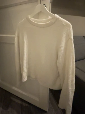 Vit fluffig stickad tröja 157 - Mysig vit stickad tröja från 157 i storlek XS. Tröjan har en fluffig och mjuk textur, rund halsringning och långa ärmar. Perfekt för att hålla värmen under kyliga dagar och enkel att matcha med olika outfits.