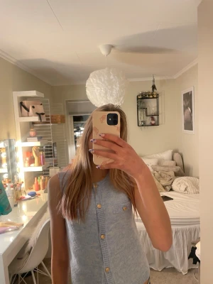 Ljusblå stickad väst med knappar - Säljer en ljusblå stickad väst med v-ringning och guldfärgade knappar framtill. Västen har en liten bröstficka och är ärmlös, perfekt att styla över en t-shirt eller skjorta för en trendig look. OBS! En knapp saknas