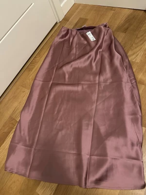 Ljuslila satinkjol från Lindex stl 170 - Säljer en  långkjol  i glansigt satinmaterial. Kjolen har en enkel och stilren design med resår i midjan för en bekväm passform. Perfekt för dig som gillar en mjuk och flowy look.