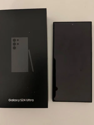 Samsung Galaxy S24 Ultra svart - Säljer en Samsung Galaxy S24 Ultra i svart med stor, kantlös skärm och stilren design. Telefonen har tunna ramar, rundade hörn och levereras med originalkartong. Perfekt för dig som vill ha en kraftfull Android-mobil med modern look.