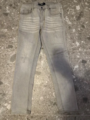 Ljusgrå slim fit jeans  - Säljer ett par ljusgrå slim fit jeans med diskreta slitningar och tvättade detaljer på låren. Klassisk femficksmodell med knappgylf och raka ben. Perfekta för en avslappnad och trendig look.