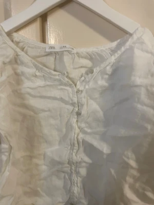 Vit blus med knappar från Zara - Har använt 2-3 gånger. Jag tycker den är storlek 145-152. Luftig vit blus från Zara med knappar framtill och rundad halsringning. Tillverkad i ett tunt, lätt material som ger en avslappnad känsla. Perfekt för en enkel och stilren look, och väldigt skön på sommaren.