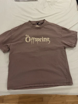 Brun The Offspring t-shirt - Säljer en brun t-shirt med The Offspring-tryck i vitt på bröstet. Klassisk rund hals och korta ärmar. Perfekt för dig som gillar bandmerch och vill ha en avslappnad stil. Storleken säger XXS men är mer än storlek S/M beroende på kroppsbyggnad