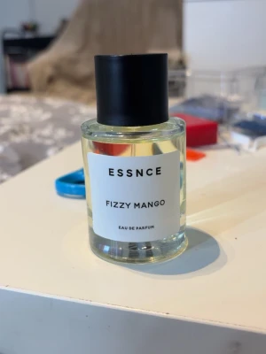 ESSNCE Fizzy Mango Eau de Parfum - Typ inget taget ur. Fräsch parfym från ESSNCE med doft av Fizzy Mango. Flaskan är cylindrisk i genomskinligt glas med svart lock och vit etikett med svart text. Perfekt för dig som gillar fruktiga och upplyftande dofter.