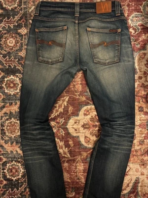 Nudie Jeans, Grim trim - Säljer dessa ass feta grim trim nudie jeans i blå färg, de finns en litet hål i skrevet men de går att skicka in till nudies egna hemsida för gratis reparation. Passformen är mellan slim och strait storleken är W 29 och L32.skriv för mer frågor eller annat✌🏻🔥