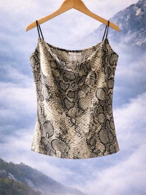 Ormmönstrat linne från Amisu - Snyggt linne från Amisu med trendigt ormmönster i svart, grått och vitt. Linnet har tunna svarta axelband och en avslappnad, draperad urringning. Perfekt för dig som vill sticka ut med ett djurmönstrat plagg.