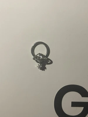 Silverfärgad septum ring  - Unik silverfärgad ring med ett planetmotiv och en liten gnistrande sten i mitten. Ringen har en rund form och detaljer som påminner om en omloppsbana och små stjärnor under planeten. Perfekt för dig som gillar rymdinspirerade accessoarer.