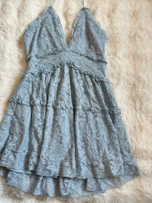 Ljusblå spetsklänning med volanger - Söt ljusblå kortklänning med spetsdetaljer och volanger. Klänningen har v-ringning, tunna axelband och omlottkänsla upptill. Perfekt för sommarens alla tillfällen. Materialet är spets med ett mjukt foder under. Köpt i usa och aldrig använd. 