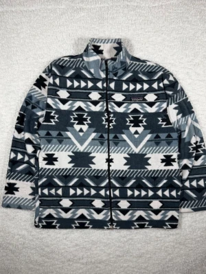 Mönstrad fleecejacka från Patagonia - Säljer en snygg fleecejacka från Patagonia i storlek M. Jackan har ett grått, svart och vitt aztekinspirerat mönster, hel dragkedja och hög krage. Tillverkad i 100% polyester, perfekt för lager-på-lager och riktigt skön att ha på sig.
