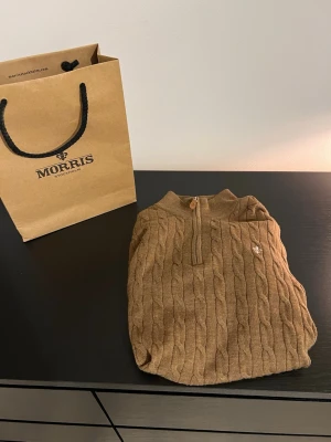 Kabelstickad tröja från Morris - Snygg brun kabelstickad tröja från Morris med halv dragkedja. Tröjan har det klassiska Morris märket. Perfekt för dig som gillar klassisk och stilren design i mjukt material.