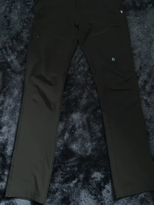 Trekmates byxor - Snygga svarta byxor med raka ben och dragkedjefickor framtill. Tillverkade i stretchigt material som sitter skönt och följer kroppen. Diskret logga på ena benet. Perfekta för en clean och stilren look.