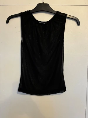 Svinsnygg glittrig topp från ONLY - Svart ärmlös topp från ONLY med glittrigt material som ger en snygg shimmer-effekt utan att bli för mycket. Tunn och lätt material, perfekt för att skapa en snygg look. Rund halsringning och slim passform som framhäver siluetten. Knappt använd, ser ny ut. Står inte storlek men skulle passas XS- mindre S